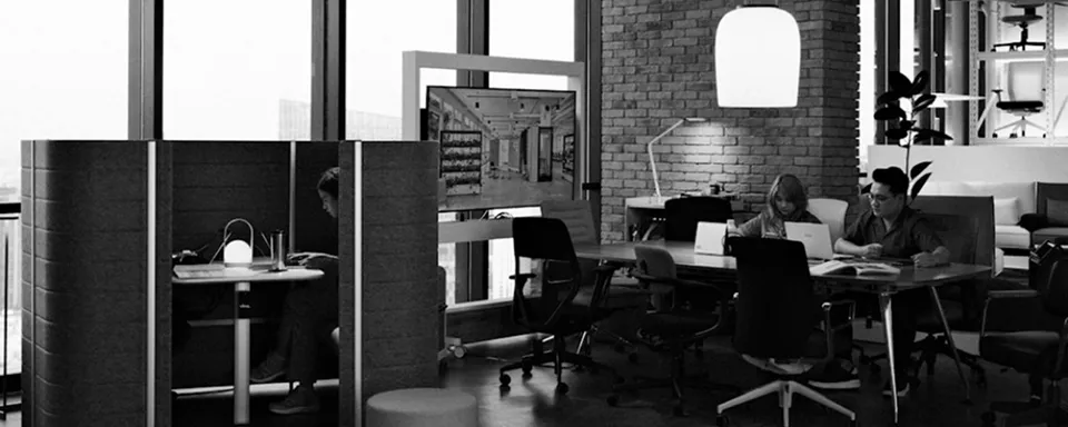 Modern office space with a person working inside a privacy pod and two others collaborating at a table with laptops.