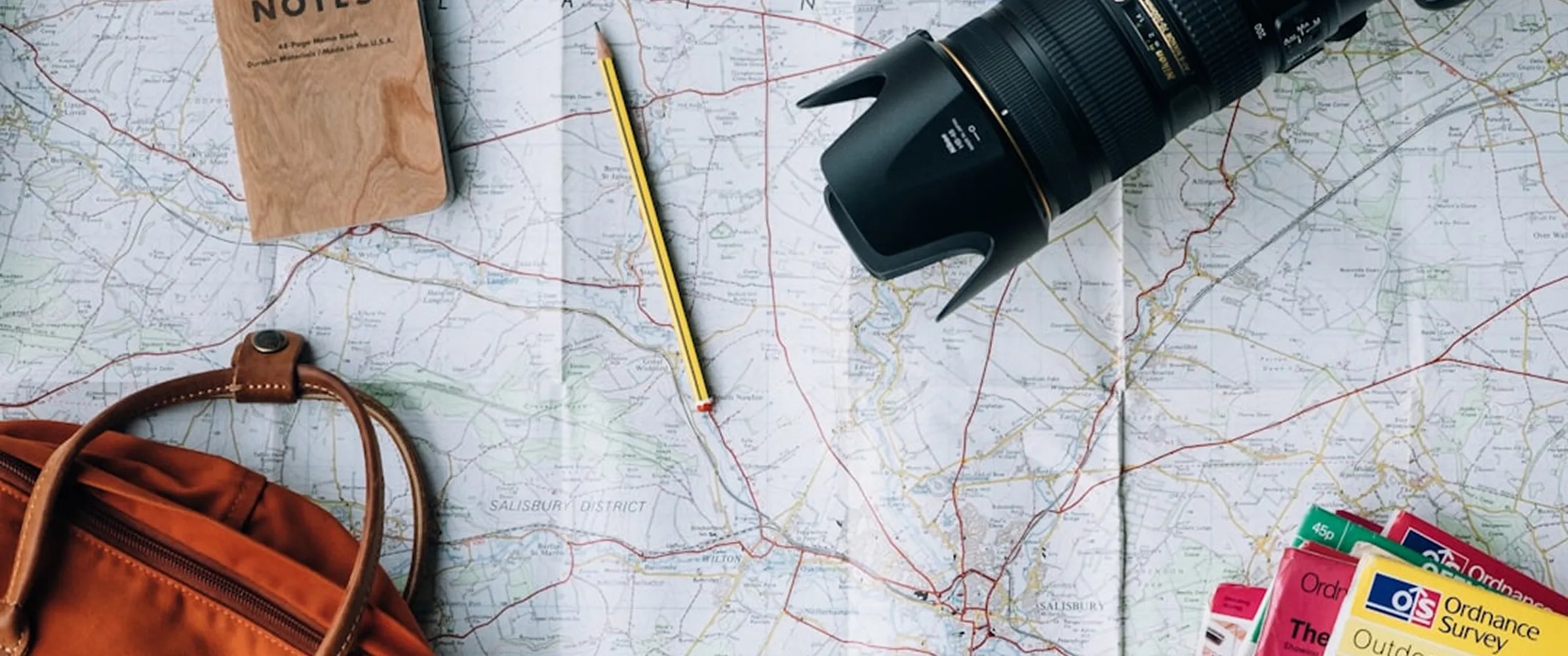 Folded map of Salisbury District with a camera lens, pencil, notebook, orange backpack, and Ordnance Survey guidebooks placed on it.