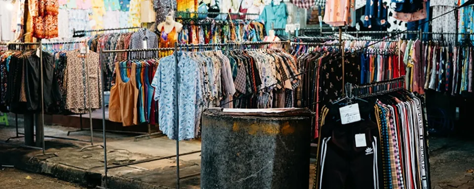 Outdoor market stall displaying various colorful shirts and tops hanging on racks.
