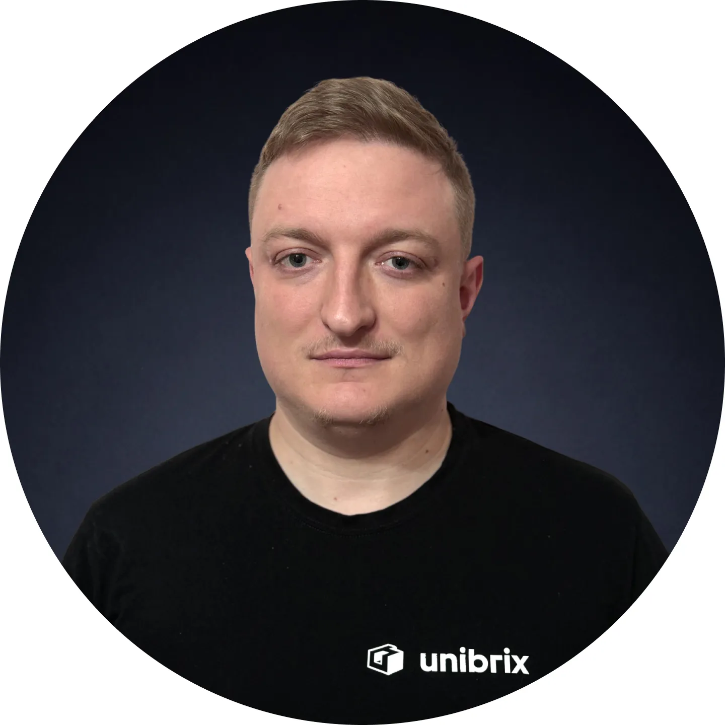 Portrait of a man with short light brown hair wearing a black T-shirt with the Unibrix logo, on a dark blue background.