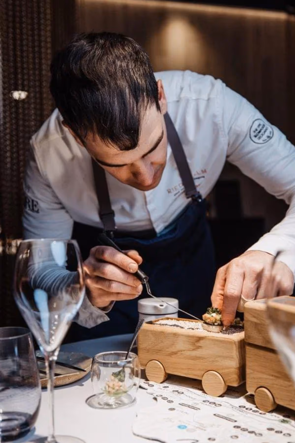 Chef carefully plating an appetizer on a wooden truck-shaped serving board in a fine dining setting.