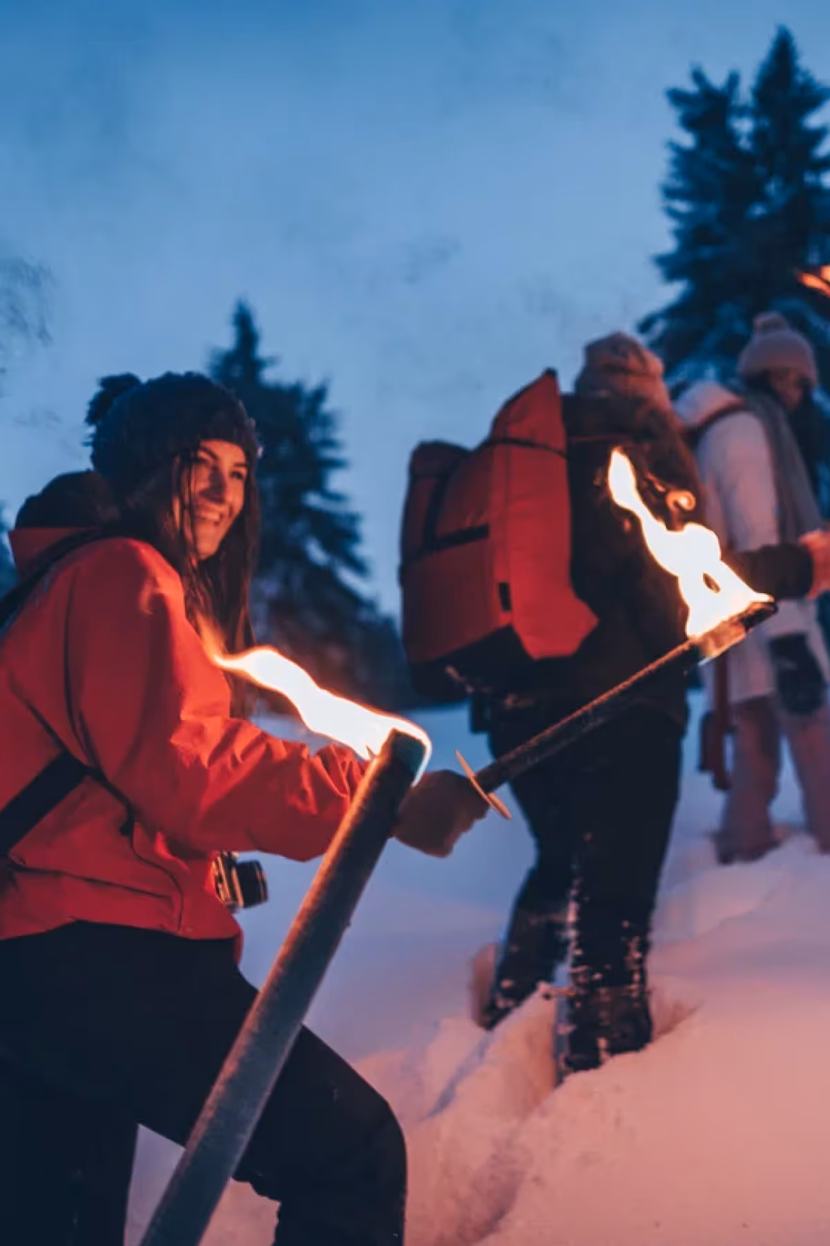 People dressed in winter clothing walking in snow at dusk, holding lit torches.