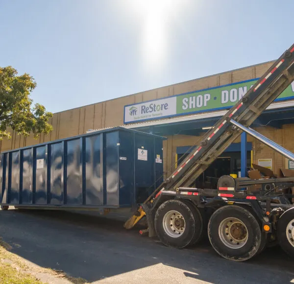 Roll-off dumpster being delivered outside a ReStore donation center for commercial waste removal and dumpster rental services.