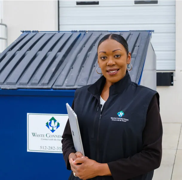 Waste service representative with tablet standing by a commercial trash dumpster.