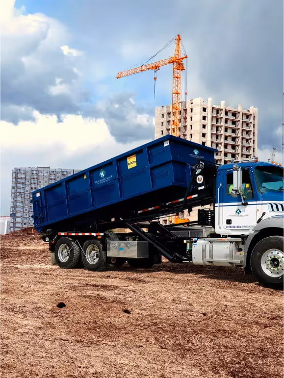 A man rolls two residential trash carts to the curb as a Waste Connections garbage truck approaches for pickup