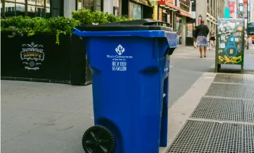 Waste service worker waving near a commercial trash dumpster at a business location.
