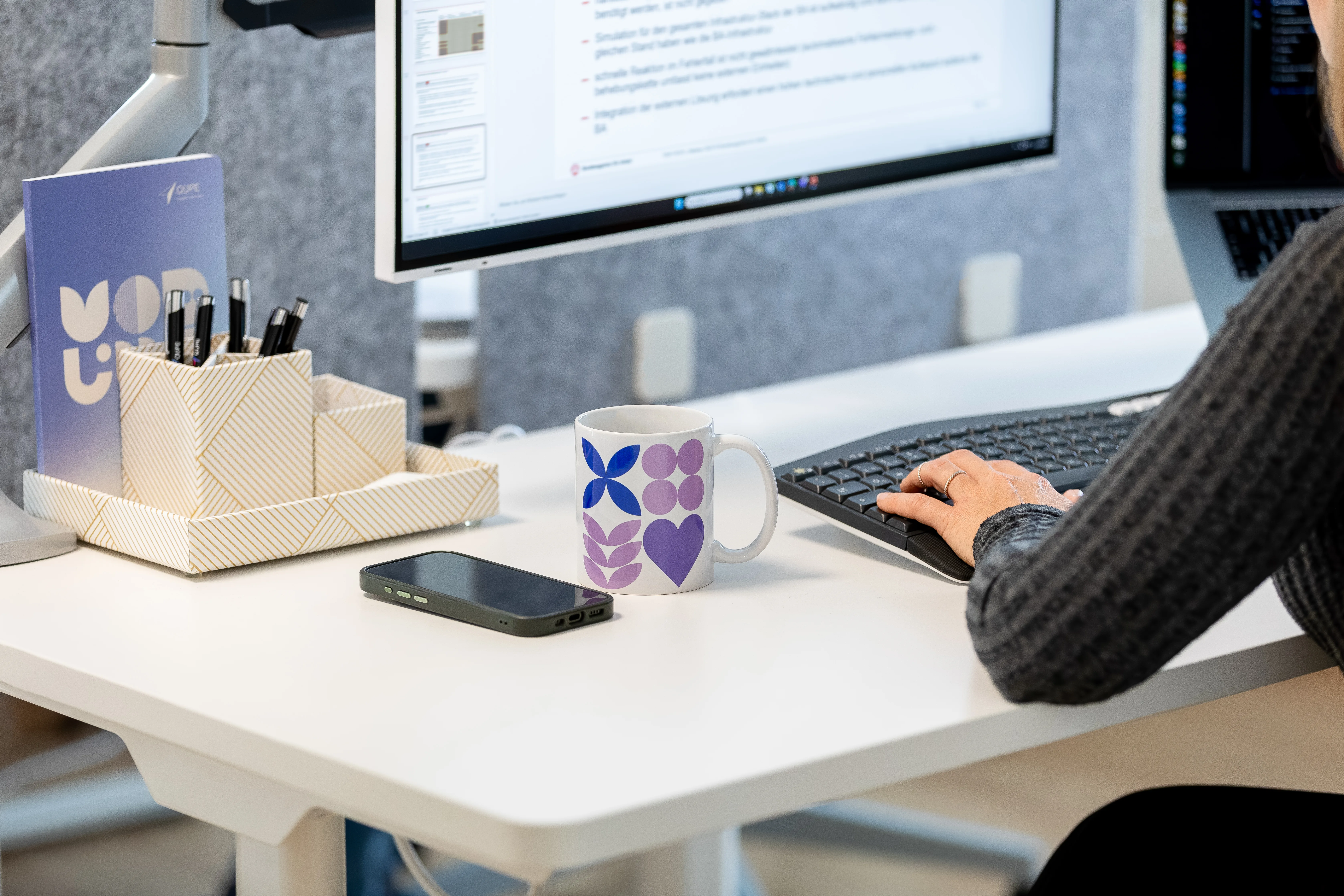 Eine QUPE-Tasse als Beispiel für Brands Tassen auf einem Schreibtisch neben einer Computermaus und Steh-Schreibtisch-Reglern