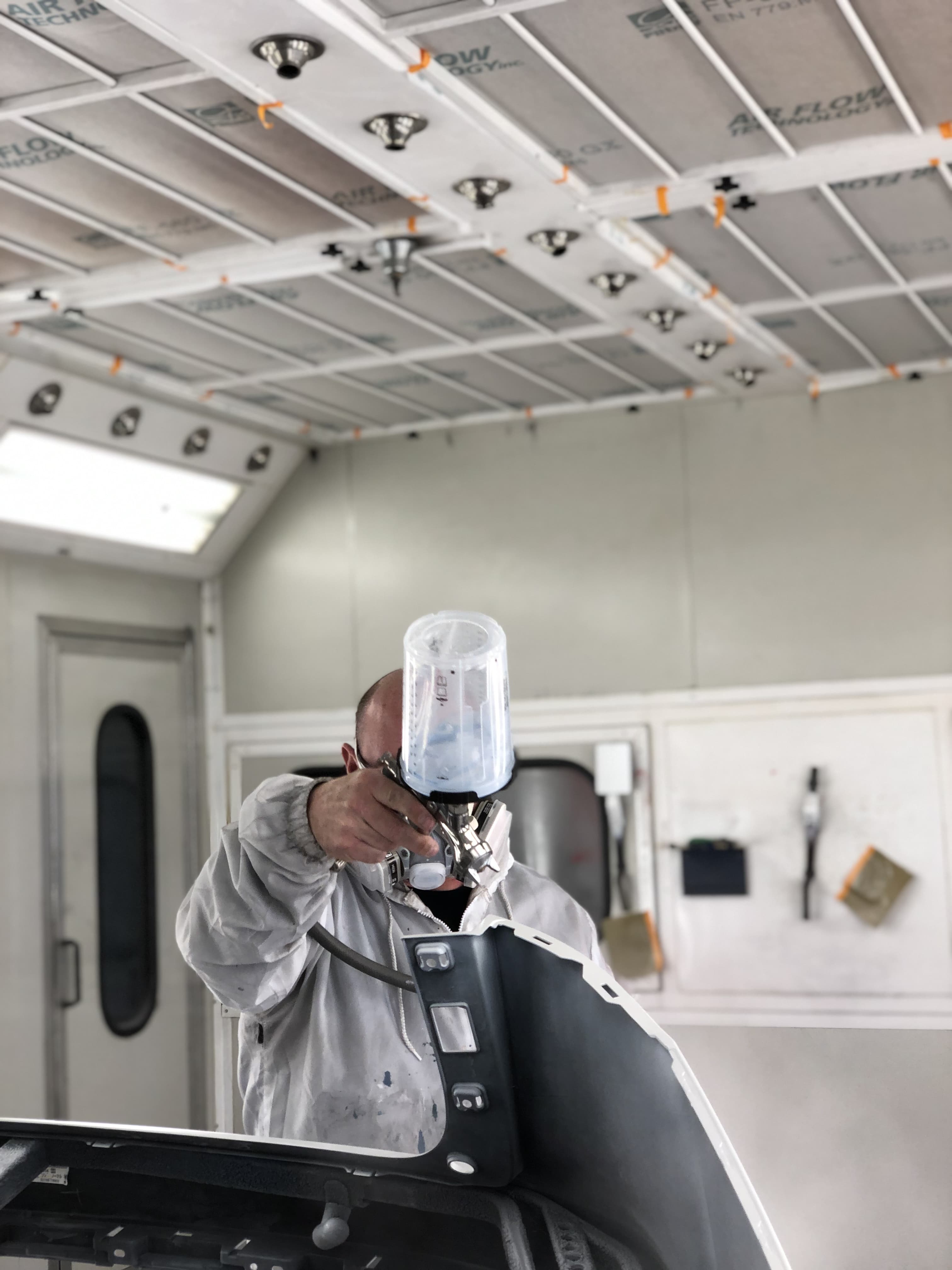 A skilled technician inspects a silver sedan in a collision repair shop, focusing on freshly repaired and primed panels. The vehicle is masked with blue tape and plastic, surrounded by auto repair tools, highlighting the detailed car restoration process after an accident.