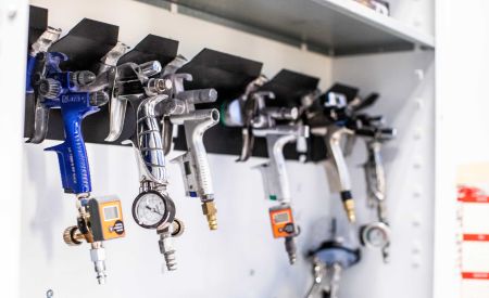 Spray guns with pressure gauges on a paint shop wall rack