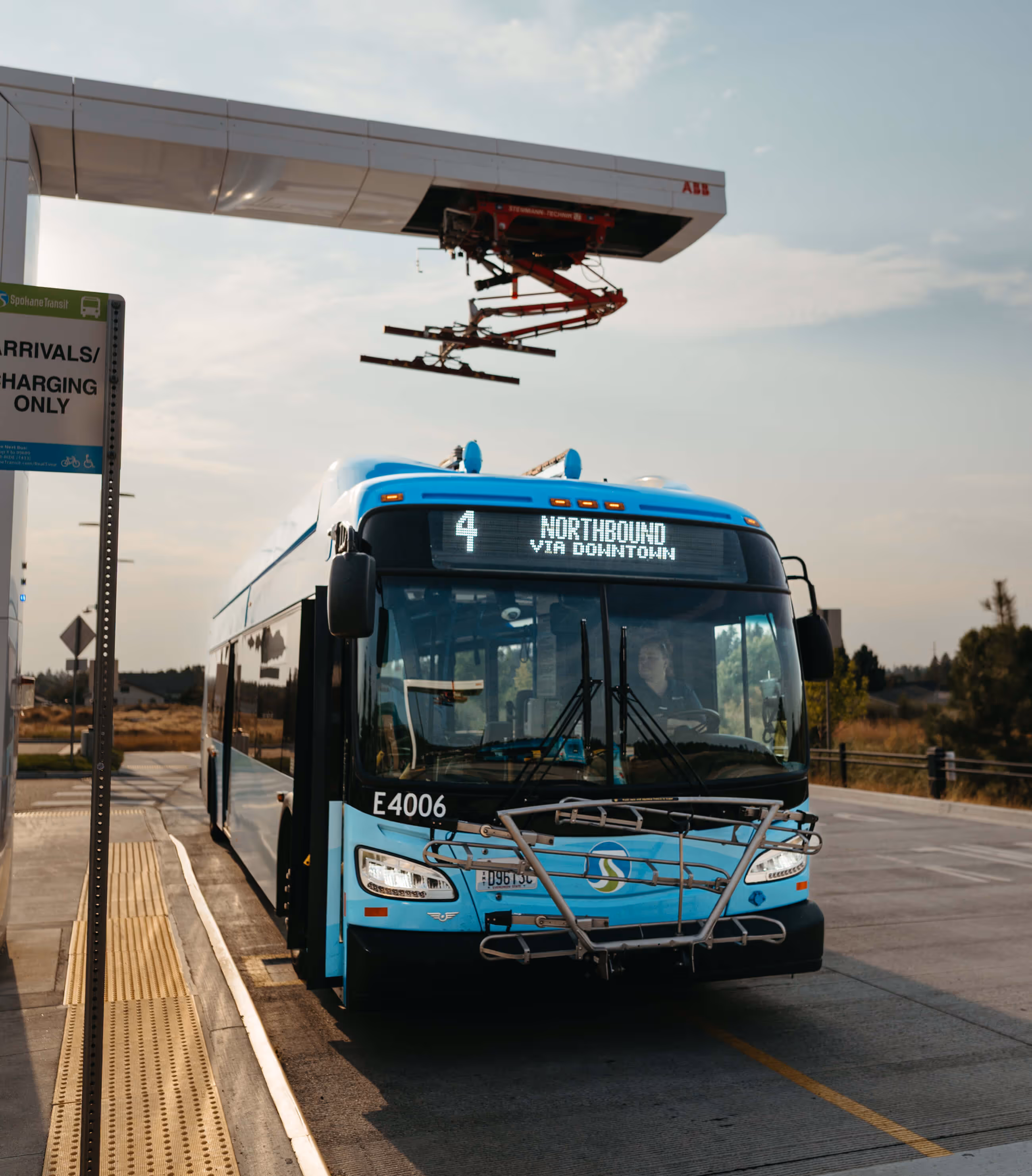 Blue Spokane Transit bus number 4 parked at a charging station with a sign indicating arrivals and charging only.