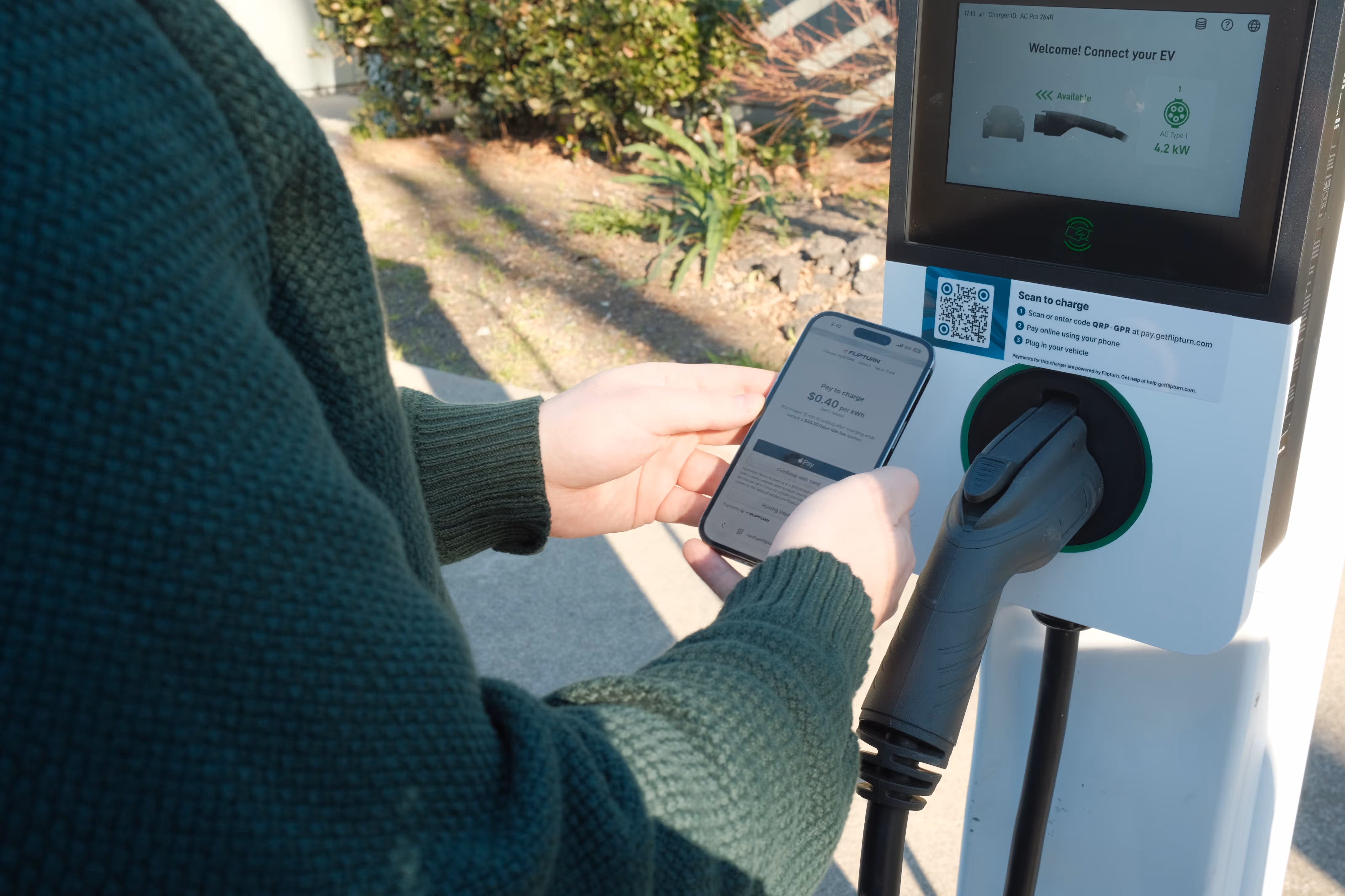 Person using a smartphone to pay at an electric vehicle charging station at the Dutton
