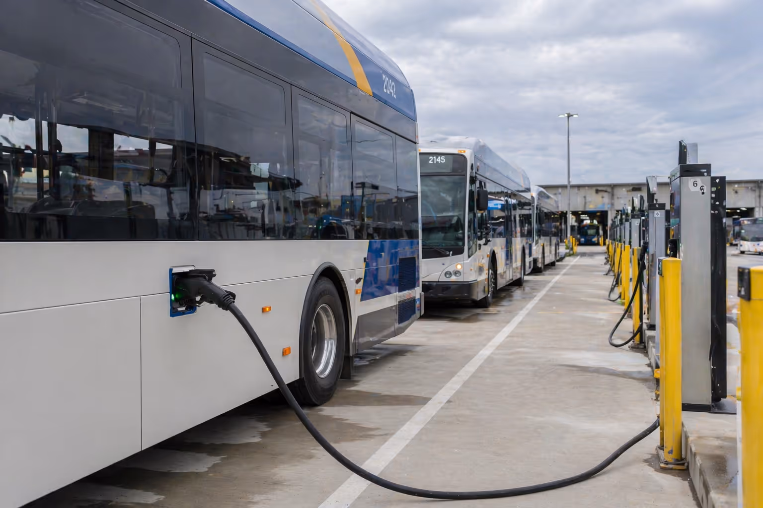 Electric transit buses lined up and charging at a bus depot with charging stations.