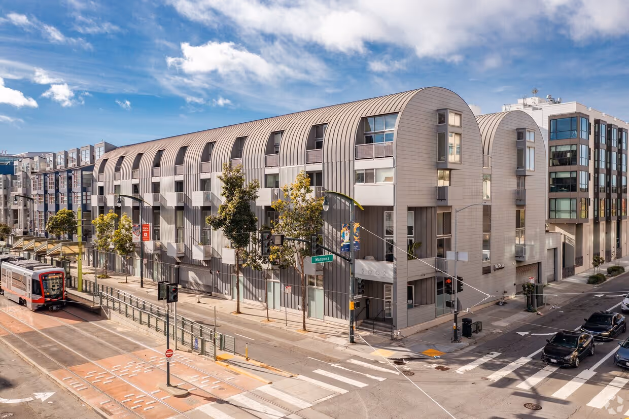 Exterior of Third Street Loft condo HOA building, shown on a sunny street corner with cars and a train nearby.