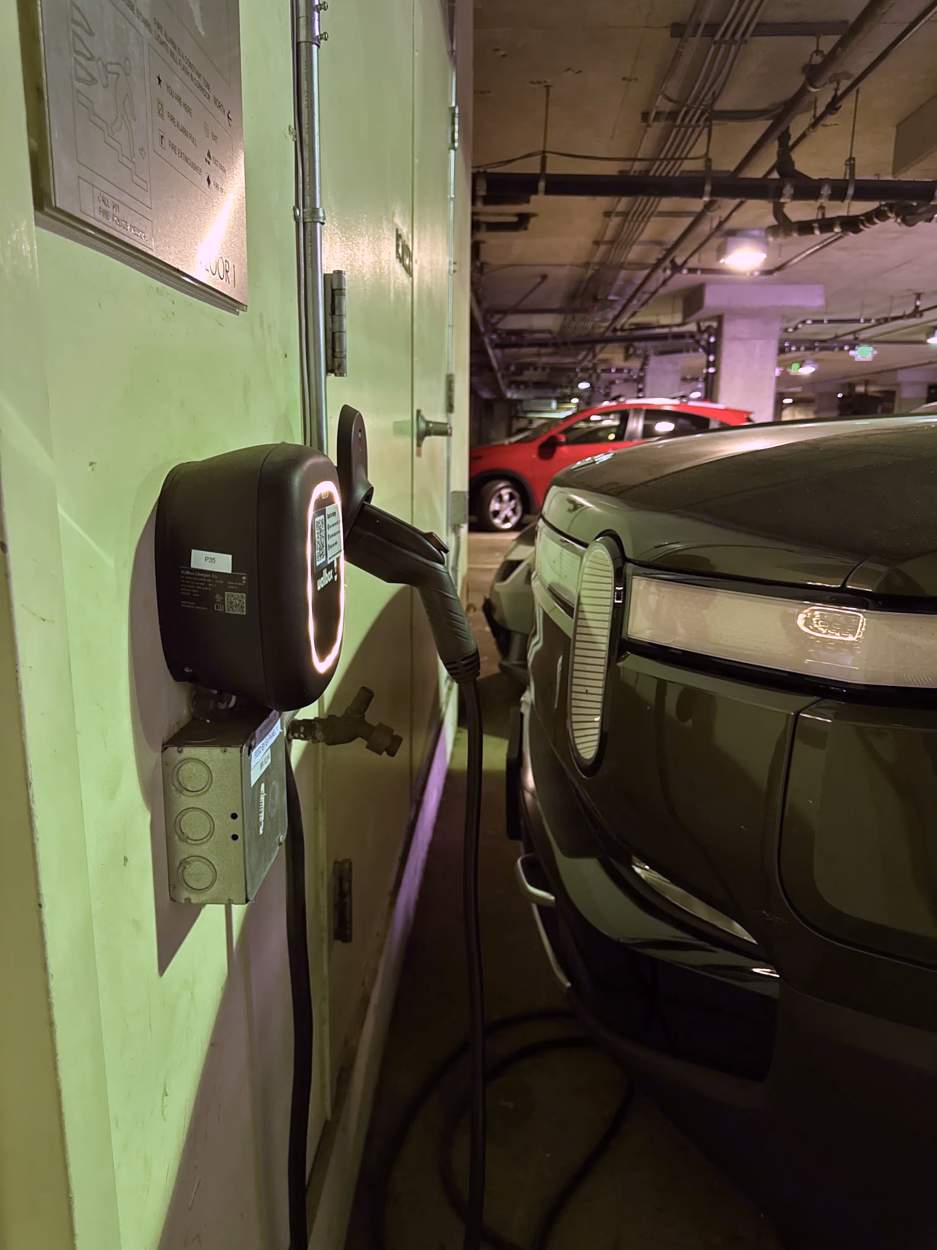 A wall-mounted Level 2 EV charger actively charging a vehicle in the underground parking garage at Third Street Lofts, San Francisco — one of 26 resident-dedicated chargers managed by Flipturn.