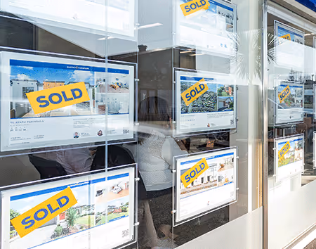 Pictures of numerous sold signs up in the window of Barfoot & Thompson Te Atatu