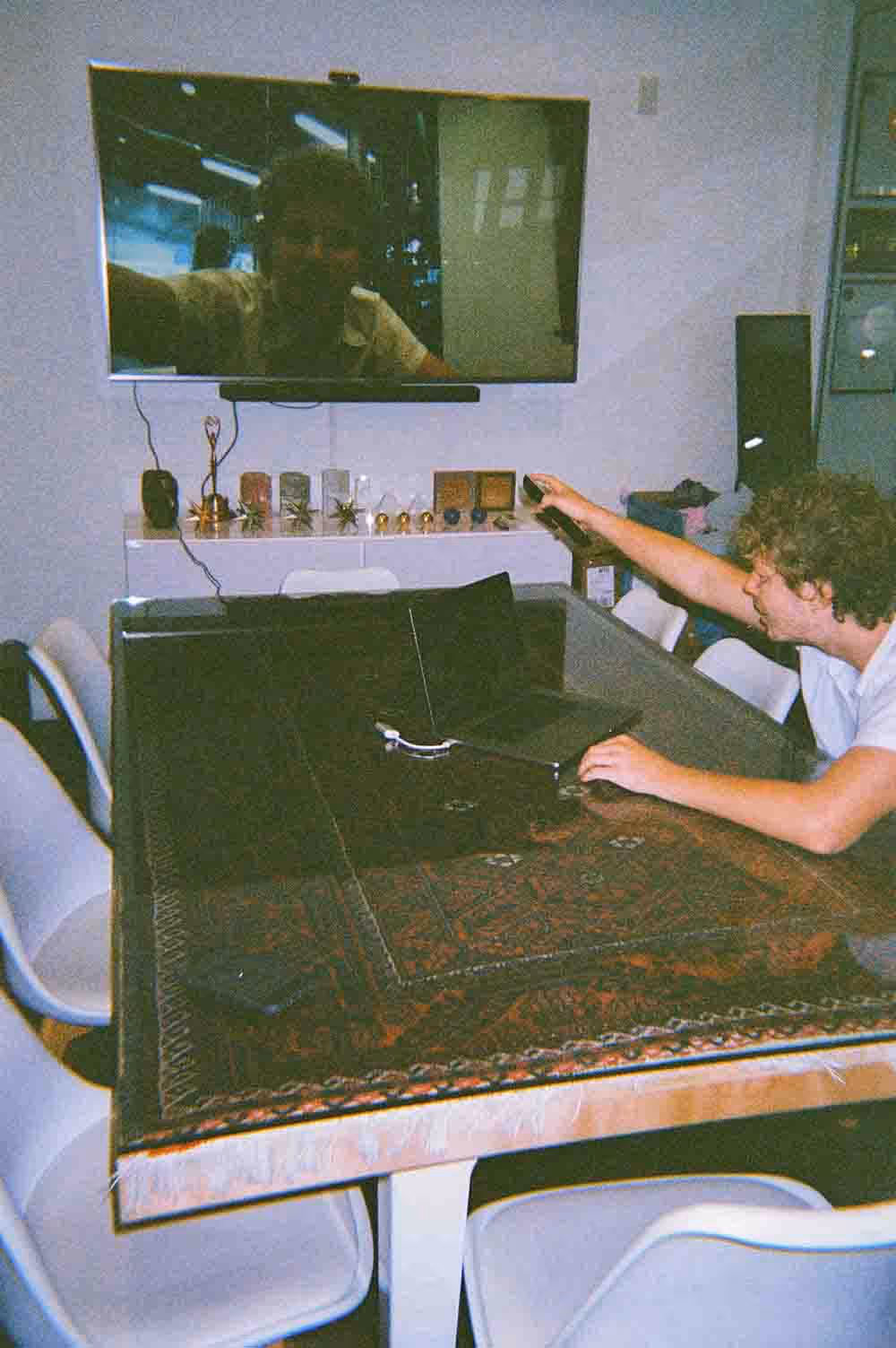 A person in a meeting room sets up a video call on a large screen, with trophies and awards displayed on a shelf behind them.