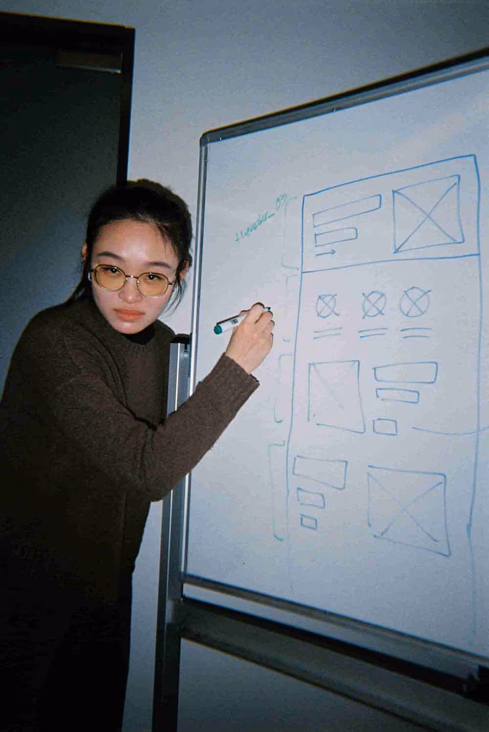 A woman sketching a wireframe layout on a whiteboard, mid-concept in a creative planning session.