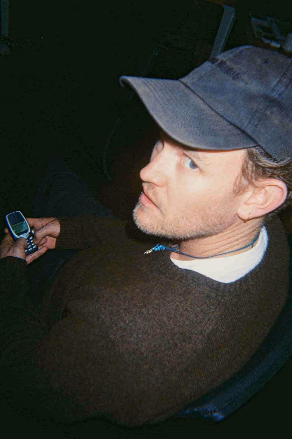 A man in a cap holding a retro mobile phone, caught in a candid moment during a creative workday.
