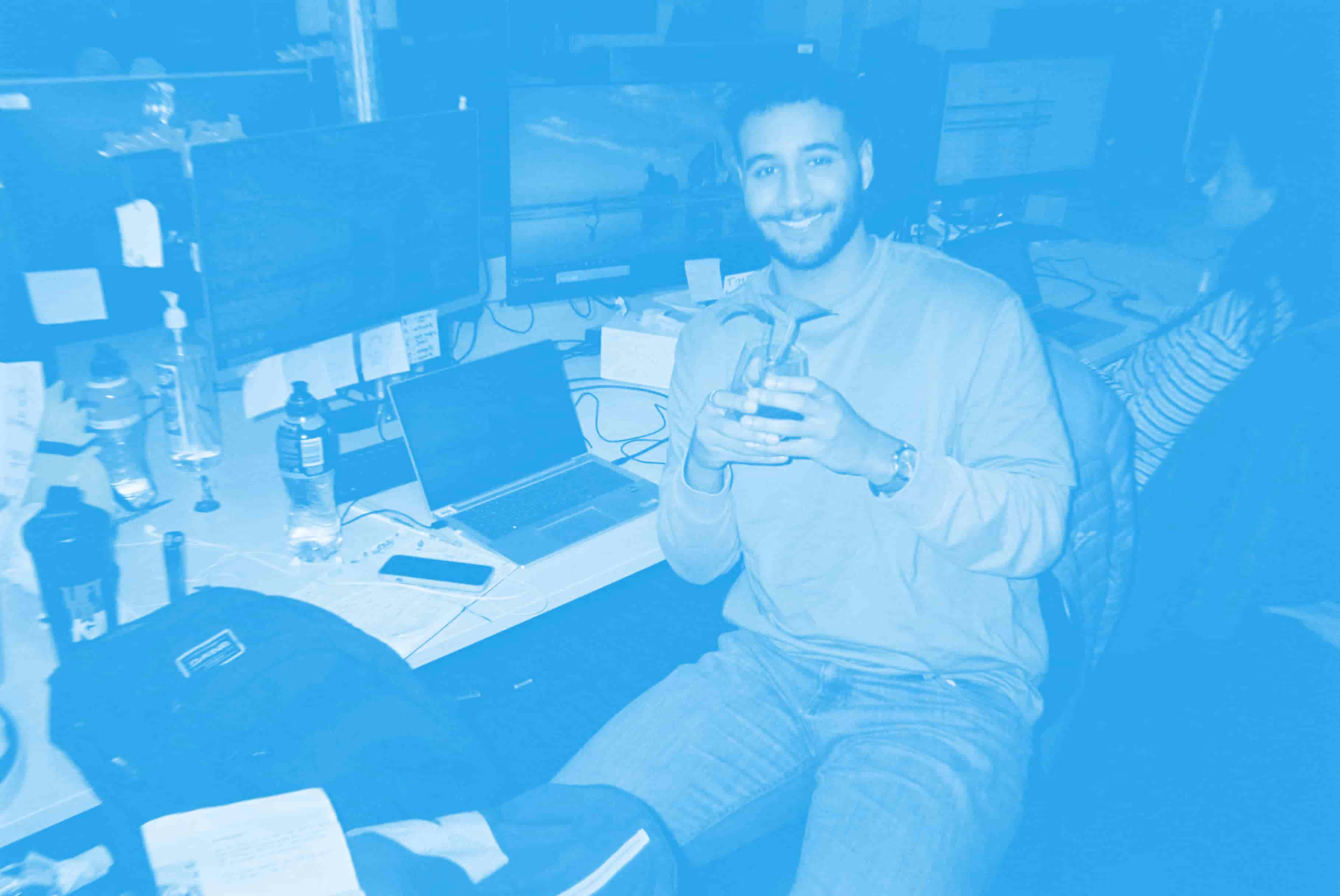 Somebody at their desk holding a drink, overlaid by a blue filter.