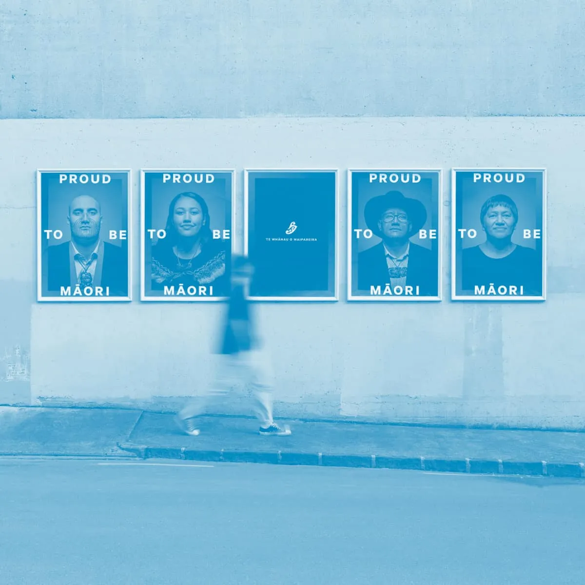 Somebody walking past printed ads for the Proud to be Māori campaign, overlaid by a blue filter.