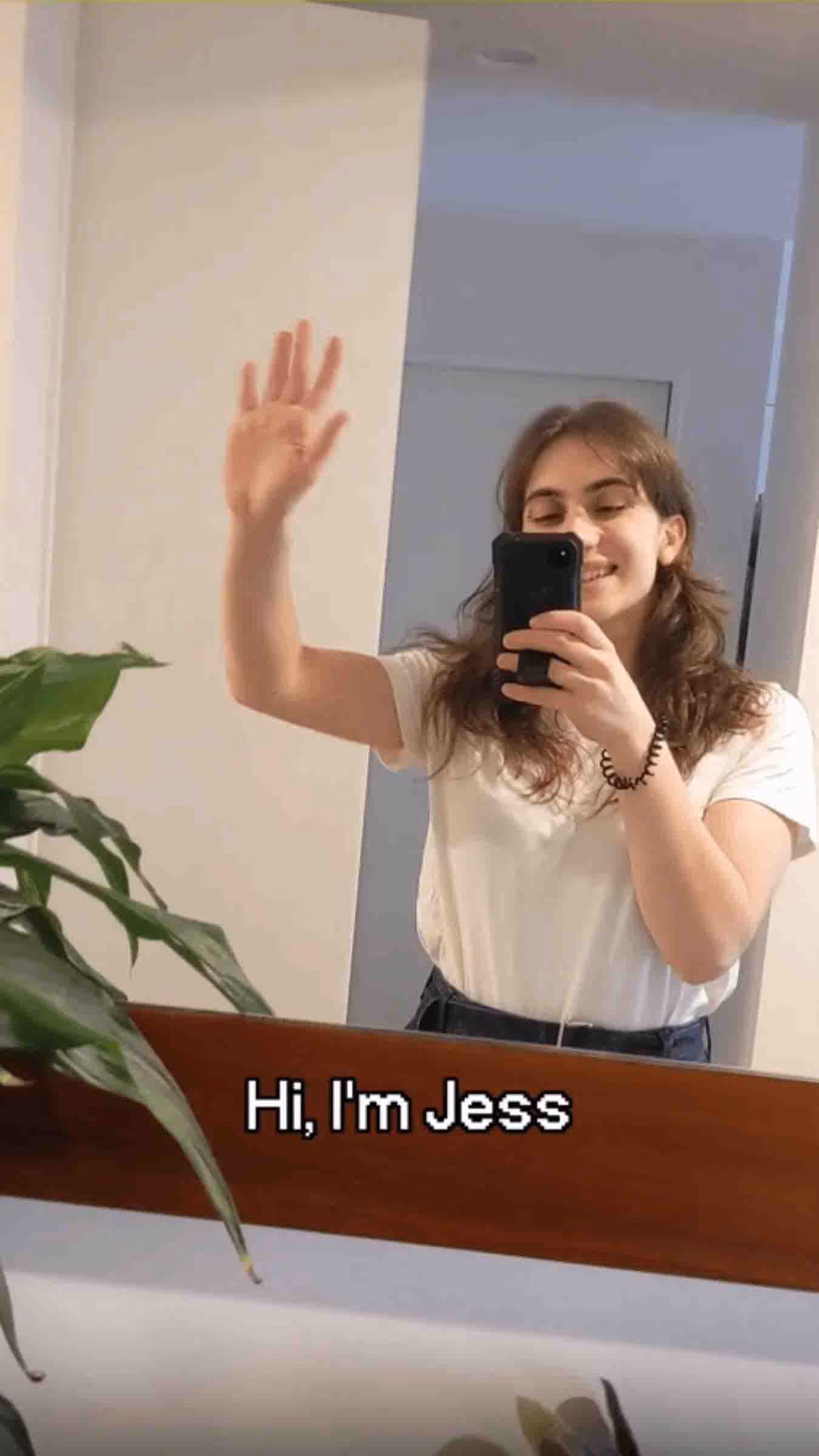 A young woman waving and taking a mirror selfie, with the on-screen text 'Hi, I'm Jess'.
