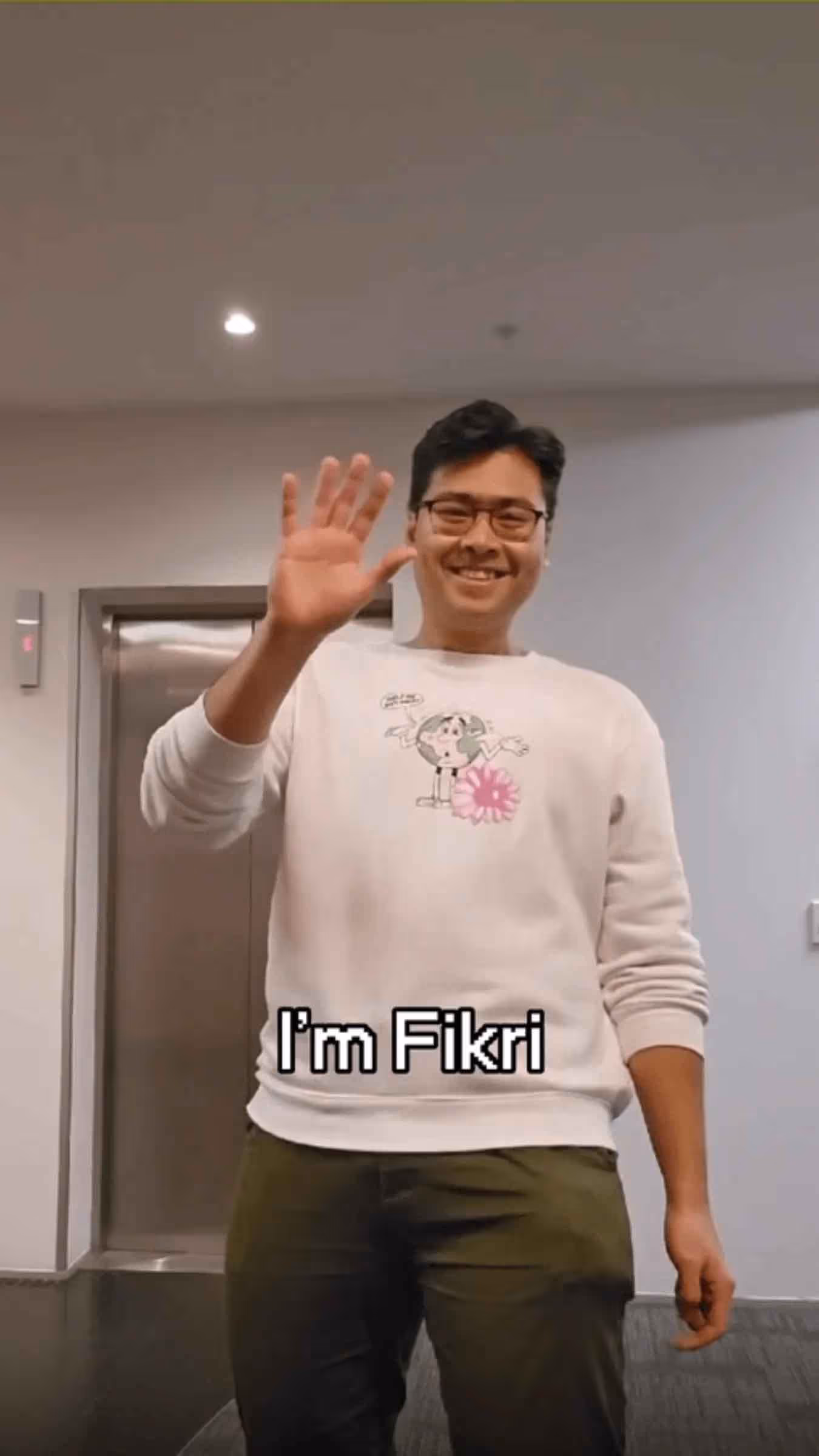 A man smiling and waving in an office hallway, with on-screen text that reads 'I'm Fikri'.