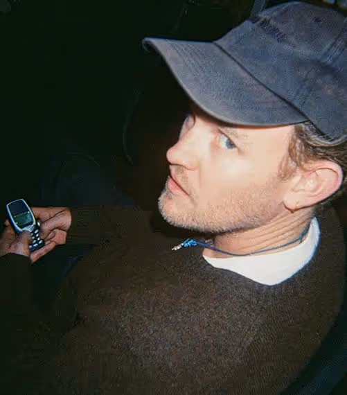 A man in a cap holding a retro mobile phone, caught in a candid moment during a creative workday.
