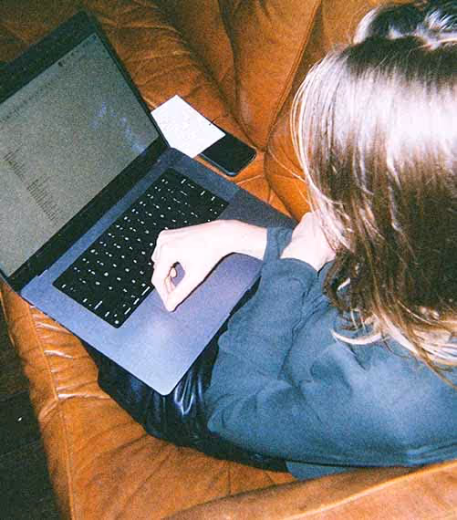 An overhead view of a woman working intently on a laptop while seated on a leather couch, reflecting focused moments in advertising roles.
