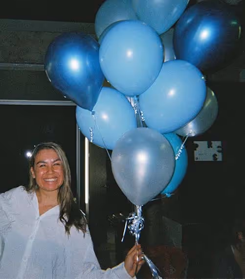 A woman smiling and holding a bunch of blue balloons at an agency event, showing the celebratory side of advertising culture.