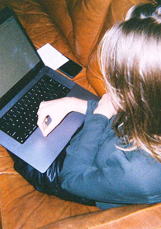 An overhead view of a woman working intently on a laptop while seated on a leather couch, reflecting focused moments in advertising roles.