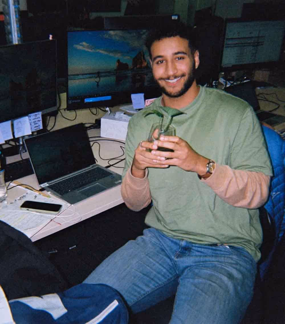 A young man in a creative office setting smiles while holding a plant, representing life inside the advertising industry.