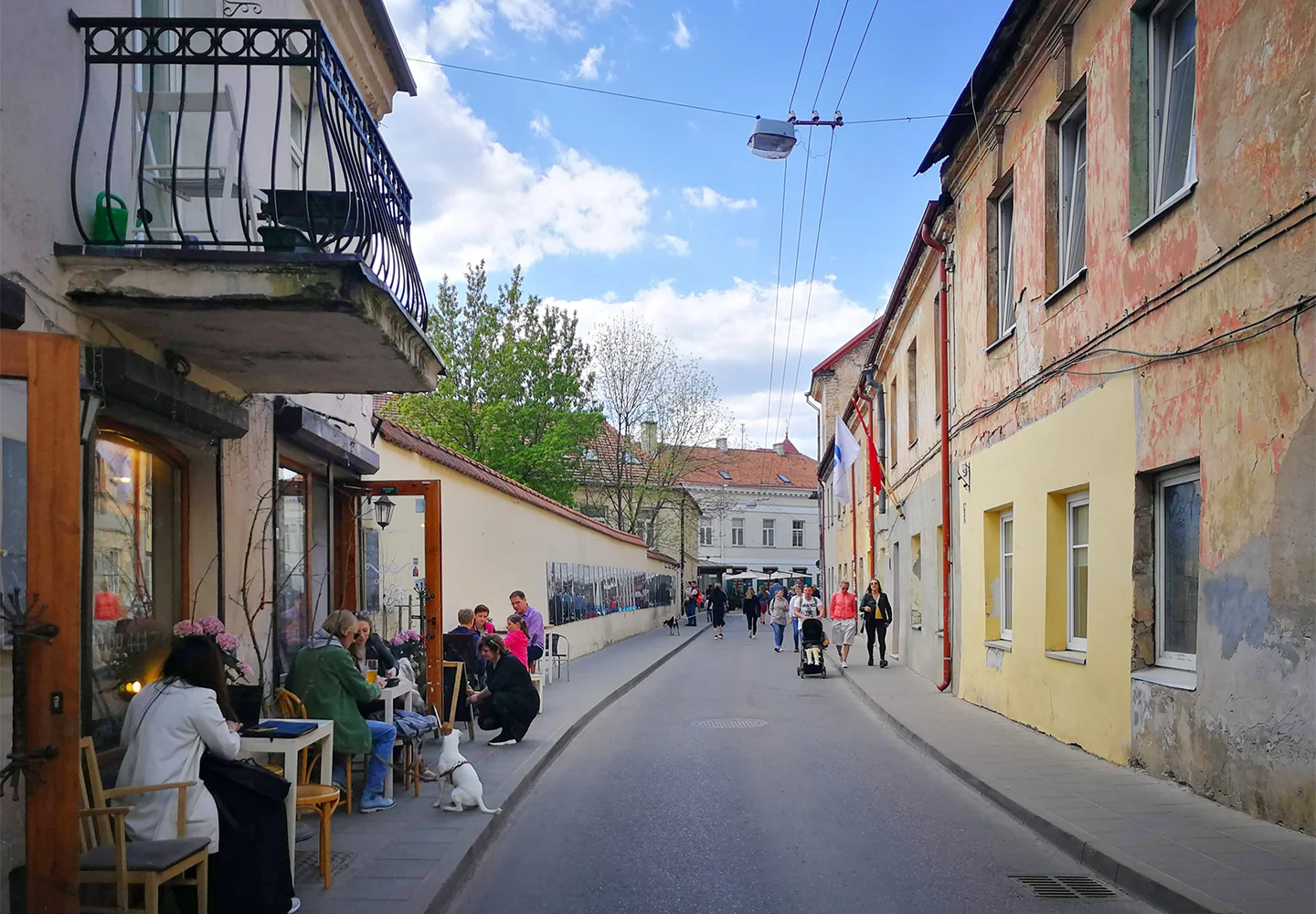 Уличка в квартал Ужупис във Вилнюс , изпълнена с хора - разхождащи се или приседнали на маси по тротоара