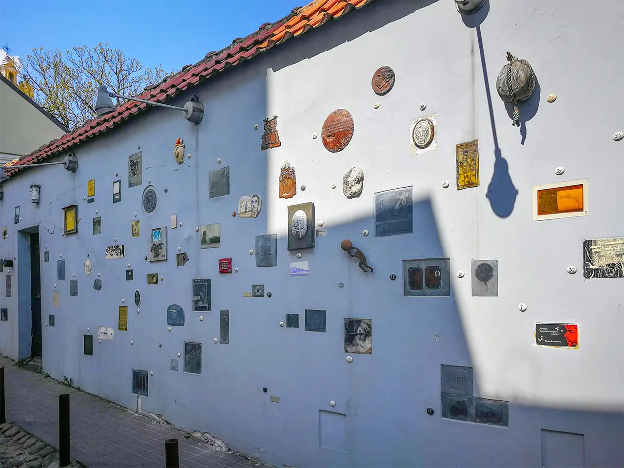 Плътна дворна ограда, окичена с разнообразни малоформатни номерирани артистични творби