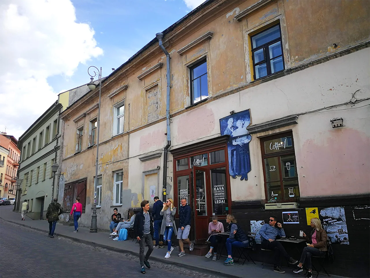 Лежерен епизод от живота по улица в Ужупис : за никъде небързащи хора край достолепно овехтели фасади на стари къщи