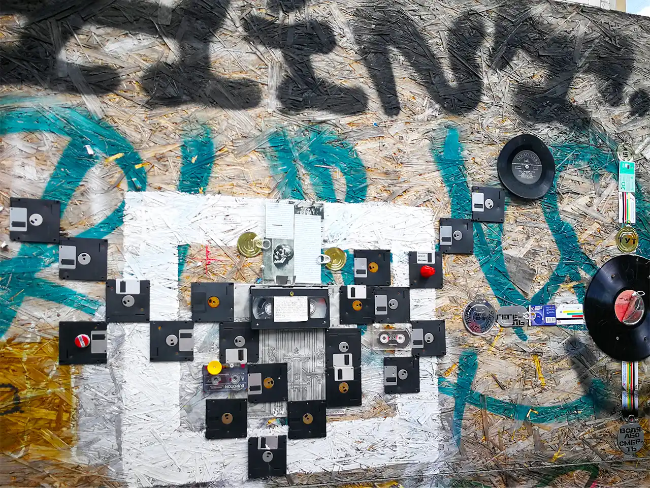 Арт композиция от дискети, видеокасети, грамофонни плочи и отпадъци от бита върху стена в градска среда