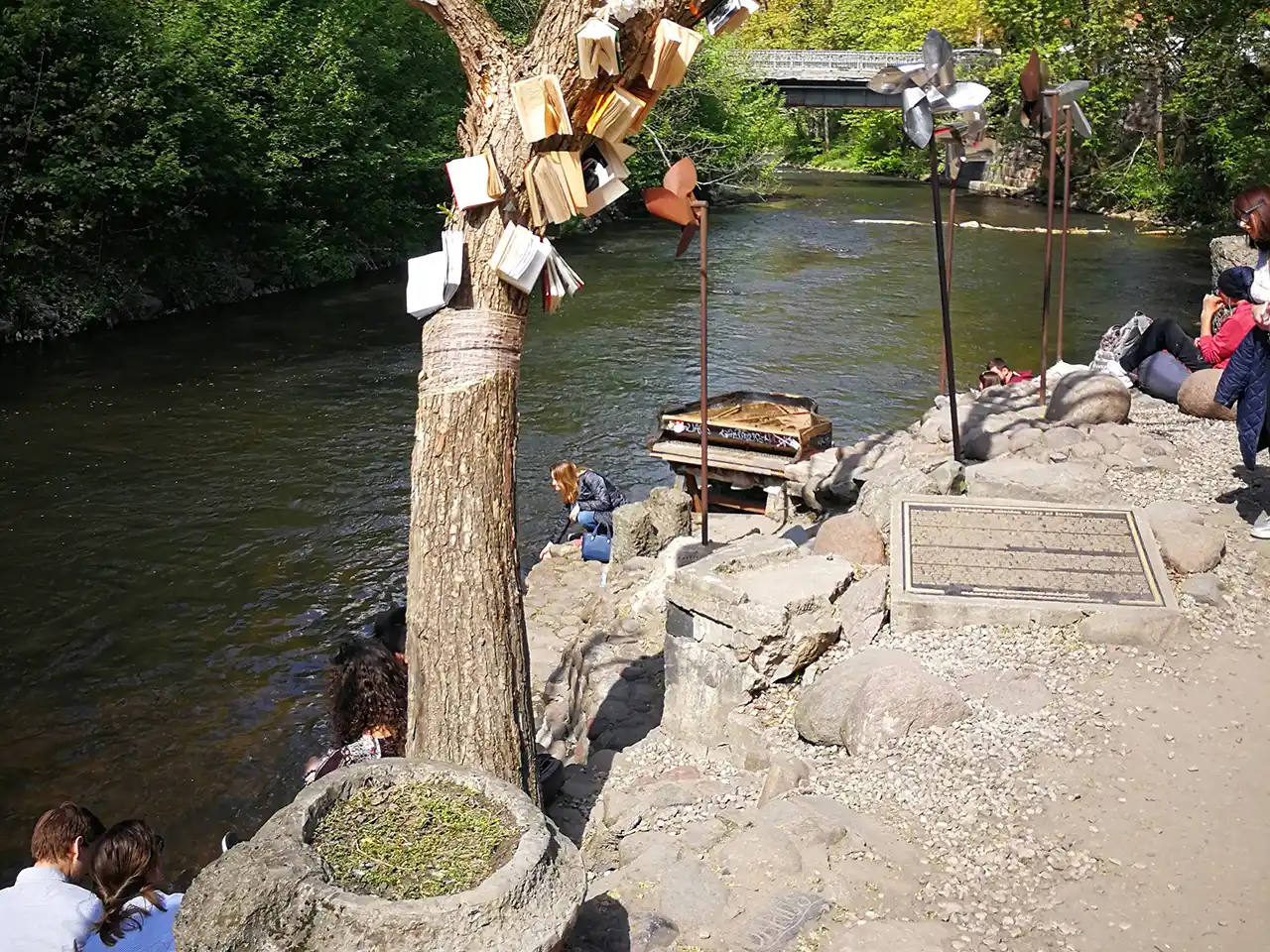 Фрагмент от крайбрежието на градска рекичка с множество любопитни арт инсталации и непринудено насядали по брега хора