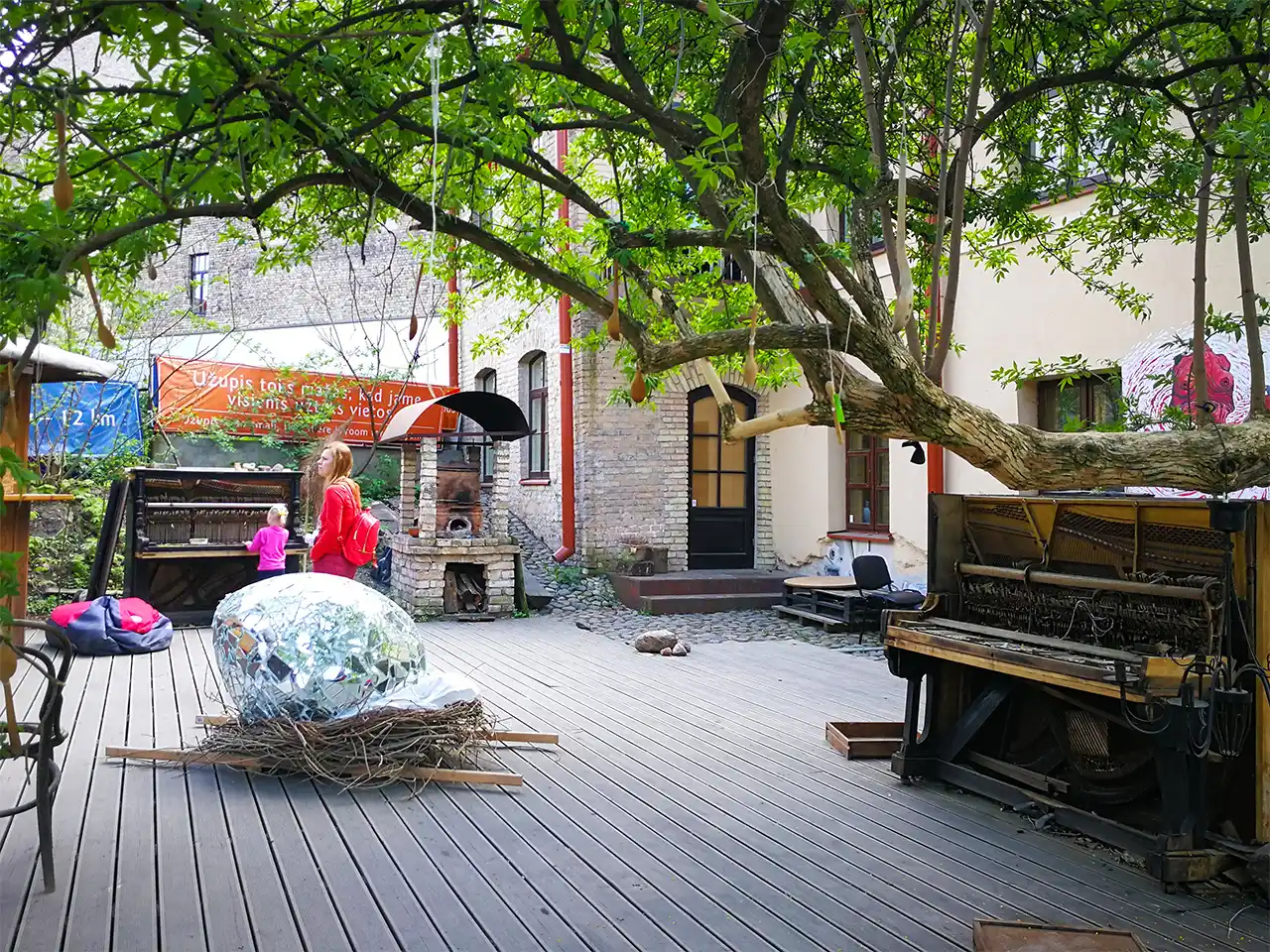 Градско пространство с полуразглобено пиано, огромно яйце от огледални фасети и висящи от клоните на дърво множество лъжици