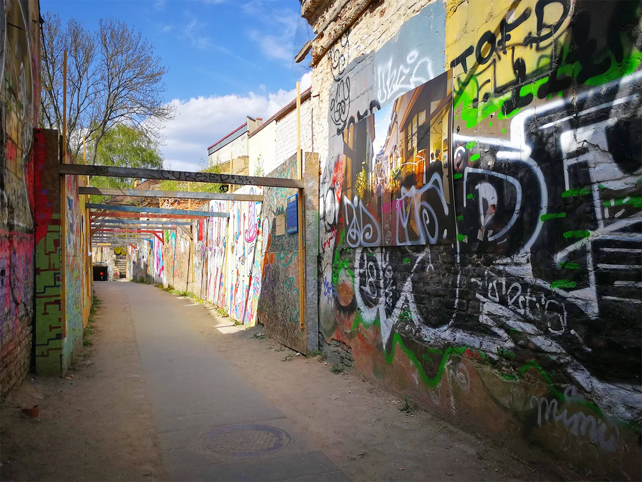 Тайнствен градски проход с пергола между две стени, изпъстрени с графити и арт творби