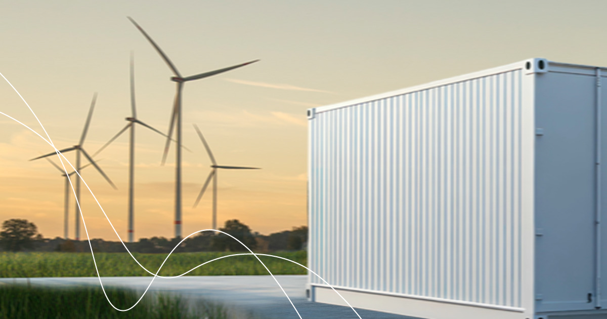 Mehrere Windkraftanlagen auf einem Feld bei Sonnenuntergang neben einem großen weißen Lagercontainer.