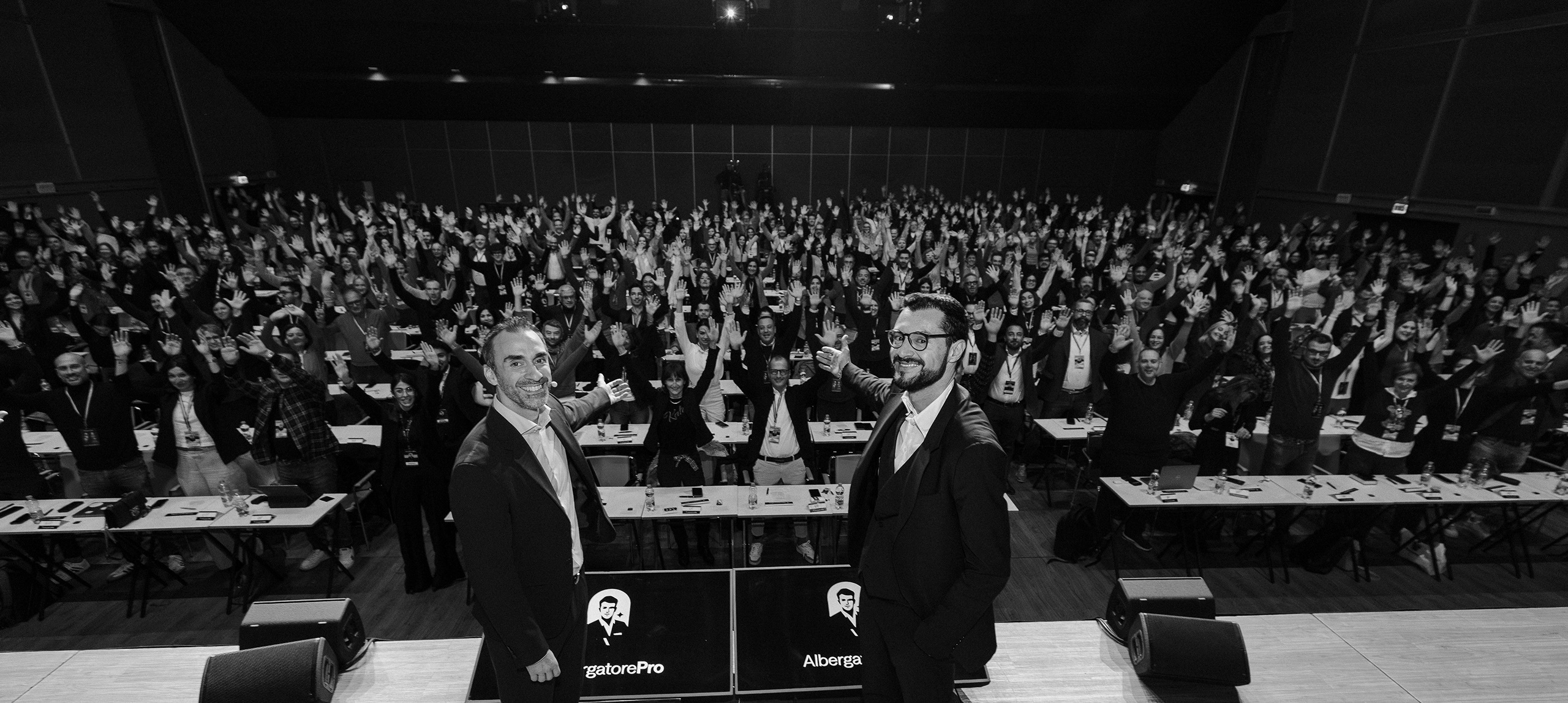 La sala di AlbergatorePro con i partecipanti a mani alzate e i due fondatori sul palco