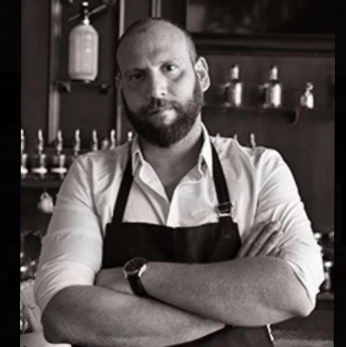 Owner and Mixologist Christos K with his cocktail creation attire on and his arms crossed.