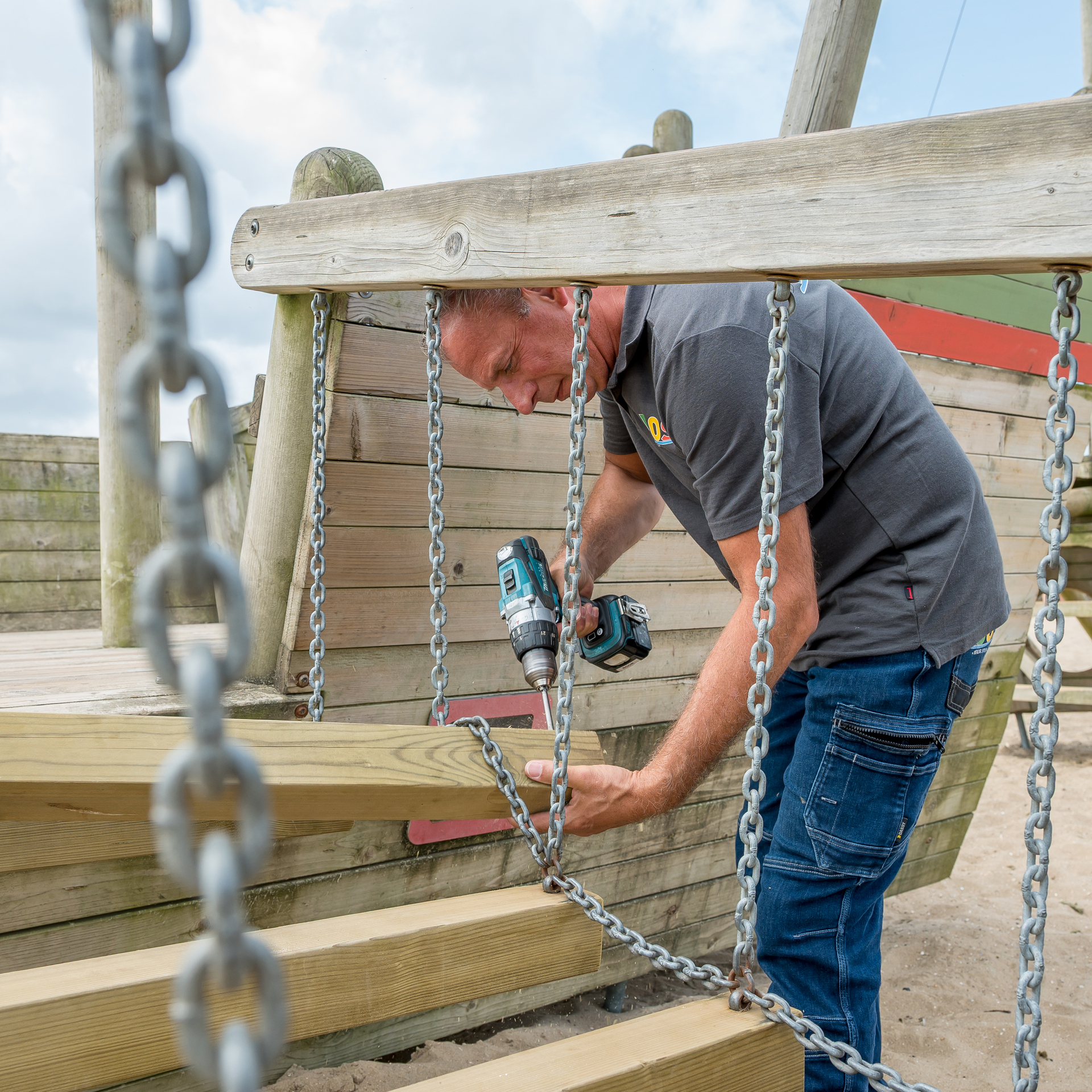 Een ABOS-medewerker staat in laagwater met een waterbestendige overall en boort een gat in een houten platform