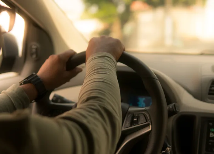 Hands on the steering wheel of a driving car.