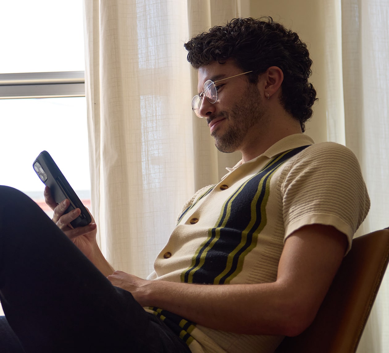 A person sits relaxed in a chair, holding a smartphone.