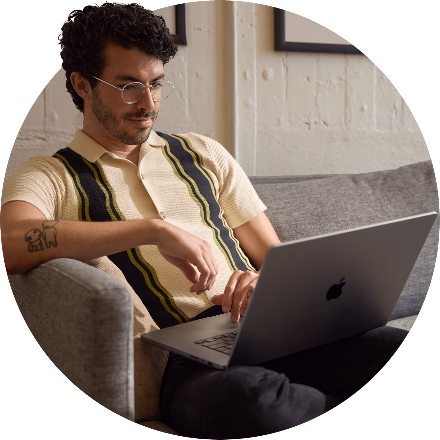 A person with curly hair sits comfortably on a gray sofa, working on a laptop.