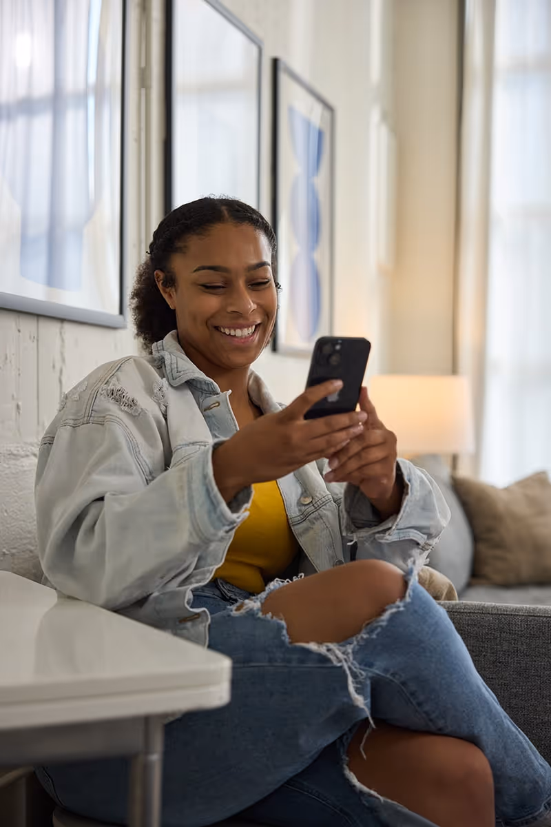 Woman sitting in her apartment, smiling at her smartphone