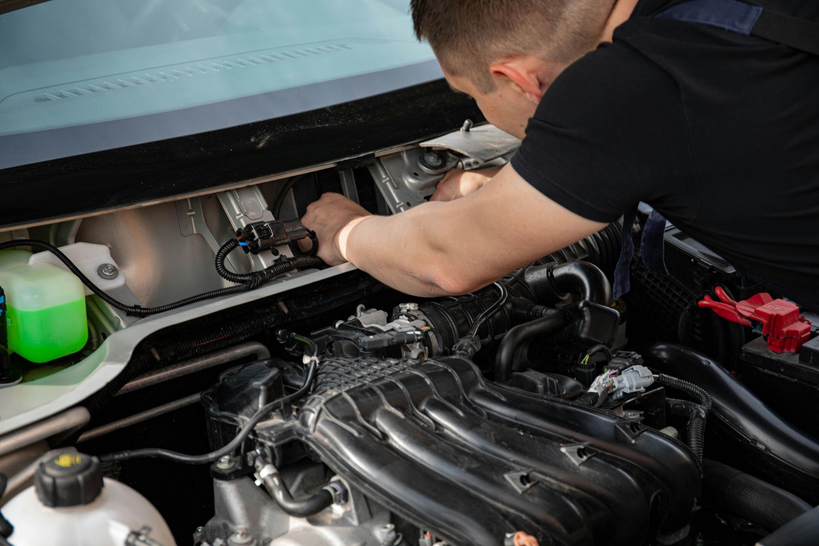 Image of a mechanic leaned over under the hood of a car to inspect or repair a part