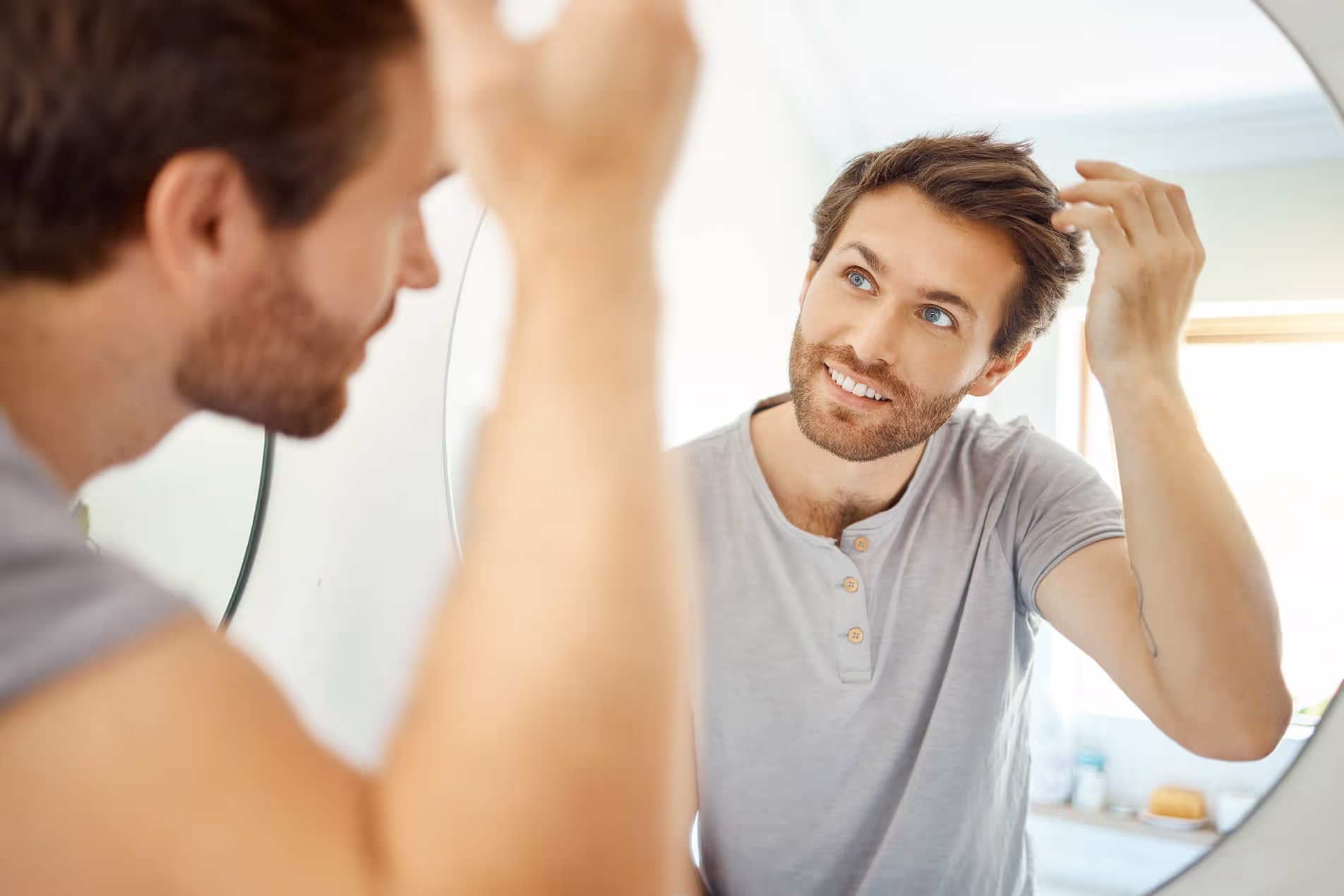 Man looking in a mirror running his fingers through his thick head of hair