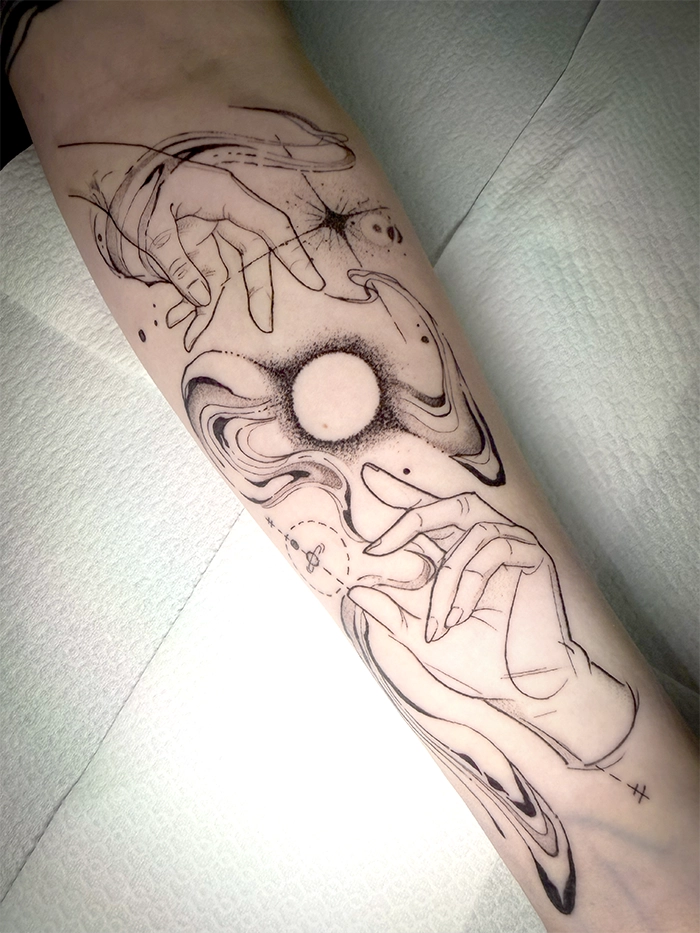 Tatoeage op onderarm met twee handen die een gloeiende bol omgeven en abstracte lijnen eromheen.