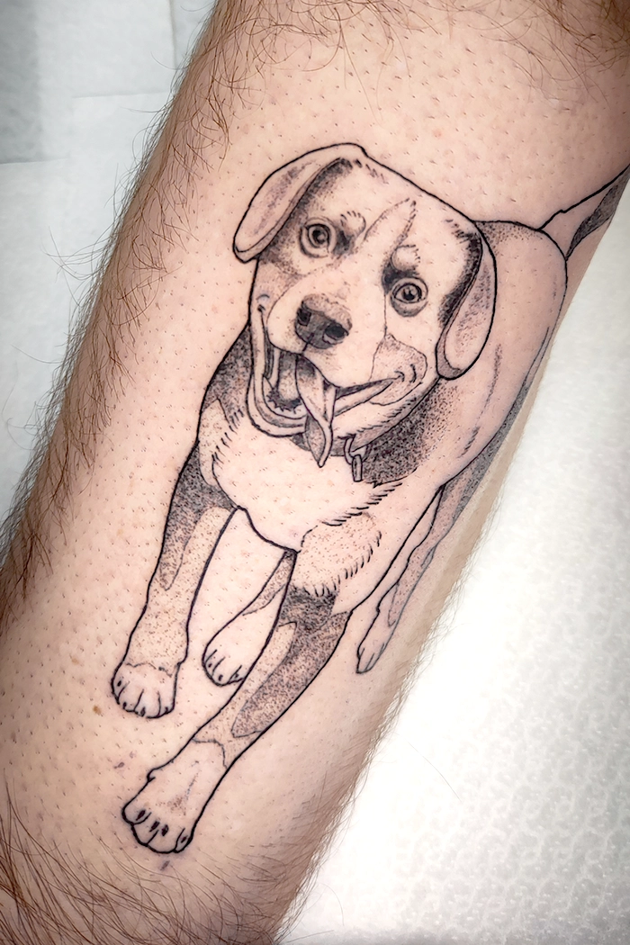 Tattoo van een blije hond met uitgestoken tong op onderarm van een persoon.